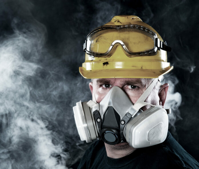 A rescue worker wears a respirator in a smokey, toxic atmosphere.  Image show the importance of protection readiness and safety.